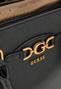 Borsa a mano in pelle nera con hardware dorato, caratterizzata da una superficie testurizzata e il logo "GUESS" ben in vista. Chiusura con zip.