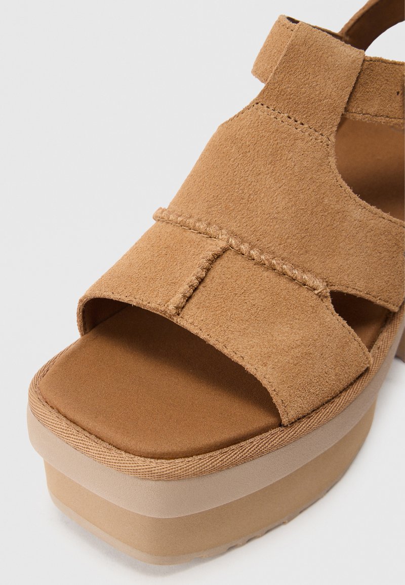Sandalia de plataforma de ante marrón con correas cruzadas, superficie texturizada y una suela gruesa de un tono claro. Cuenta con una plantilla acolchada para mayor comodidad.