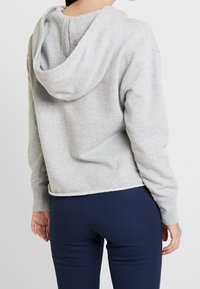 Sudadera gris corta con capucha y mangas largas, hecha de un tejido suave. Presenta un diseño simple con un dobladillo que llega a la cintura.
