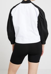 Svart och vit bomberjacka med puffig design. Den vita panelen sträcker sig över ryggen, medan ärmarna är svarta. Matchad med svarta shorts.