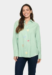 Camicia a righe verdi con maniche lunghe, caratterizzata da forme ricamate giocose e dettagli a sole. Tessuto morbido con una vestibilità rilassata.