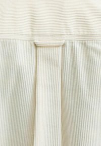 Close-up van een lichtbeige ribbelstof met een verticale band die is genaaid op een horizontale banddetail.