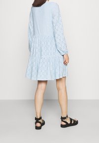 Abito di cotone azzurro chiaro con maniche lunghe, decorazioni a foro, volant a strati sull'orlo, abbinato a sandali neri con cinturini.