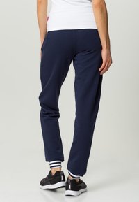 Navy sweatpants made of soft fabric with a relaxed fit. Cuffed at the ankles with white stripes. Worn with black athletic shoes.