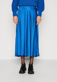 Sininen satiini midi-hame, jossa on sileä tekstuuri, virtaava muotoilu ja hieno kiilto, yhdistettynä mustiin paksupohjaisiin kenkiin.