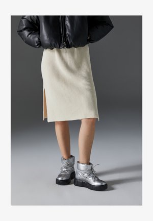 Jupe en tricot côtelé crème avec une fente sur le côté, associée à des bottines métalliques argentées avec une semelle épaisse et une finition texturée.