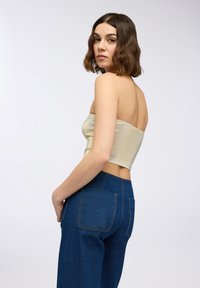 Top bez ramiączek w metalicznym złotym kolorze o dopasowanym kroju, w zestawieniu z ciemnoniebieskimi dżinsami z wysokim stanem z dwiema tylnymi kieszeniami.
