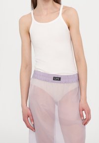 Valkoinen puuvillainen t-paita yhdistettynä läpikuultaviin lilanvärisiin housuihin, joissa on kerätty vyötärö ja musta "LPS" -labeli.