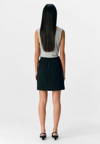 Falda negra bordada con cintura elástica, combinada con una camiseta sin mangas gris ajustada. Cabello oscuro largo visible desde atrás.