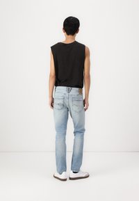 Jeans de mezclilla azul claro con corte recto, con bolsillos traseros y una marca de cuero marrón claro, combinados con una camiseta sin mangas negra.