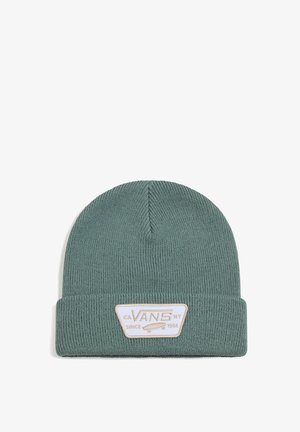 Bonnet en tricot vert avec une texture côtelée et un revers replié. Présente un patch rectangulaire blanc avec du texte et un graphique de skateboard.