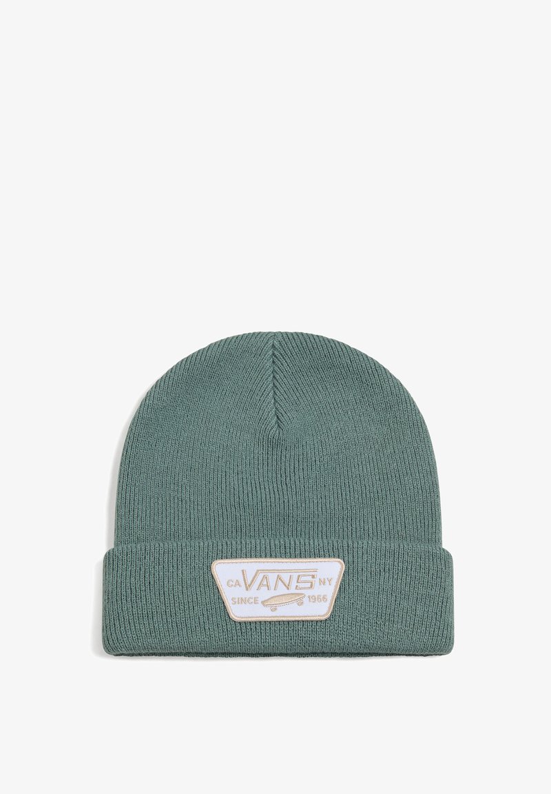 Un berretto di maglia verde con texture a coste e risvolto. Presenta una toppa bianca rettangolare con testo e un grafico di skateboard.