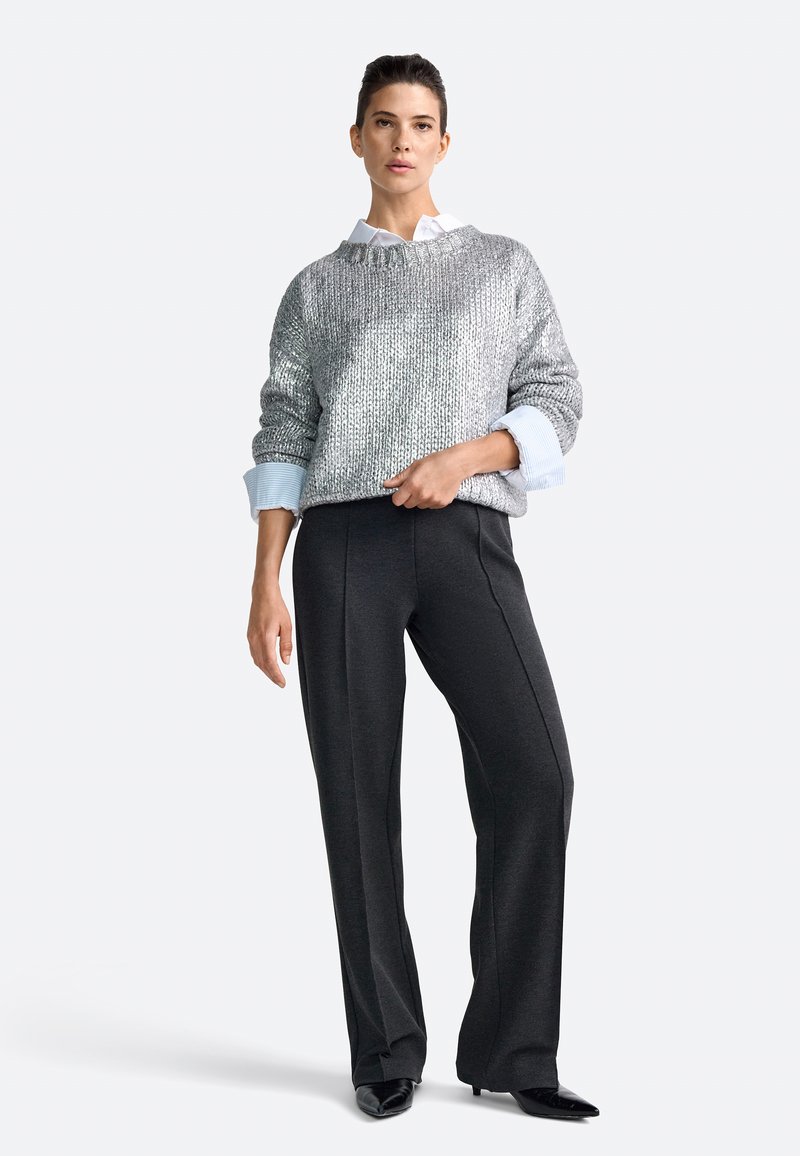 Srebrny metaliczny sweter o luźnym kroju, z prążkowaną fakturą, noszony na białej koszuli z kołnierzykiem. Dopasowany do spodni w kolorze ciemnoszarym, z wysokim stanem.