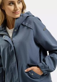 Niebieska, lekka kurtka z kapturem, zapinana na zamek błyskawiczny, z elastycznymi mankietami i bocznymi kieszeniami. Wykonana z gładkiego, wodoodpornego materiału.