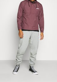 Rood en zwart geblokt hoodie met een logo, gecombineerd met grijze joggingbroek en zwarte high-top sneakers met witte zolen.