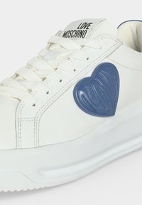 Baskets blanches à lacets avec un patch bleu en forme de cœur sur le côté et « Love Moschino » imprimé sur la languette.