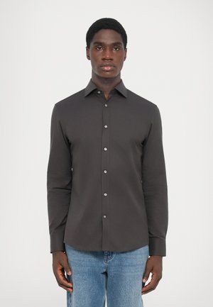 Dark grey button-up shirt with a collar, long sleeves, and a tailored fit. Features metallic buttons and a smooth texture. Worn with blue jeans.