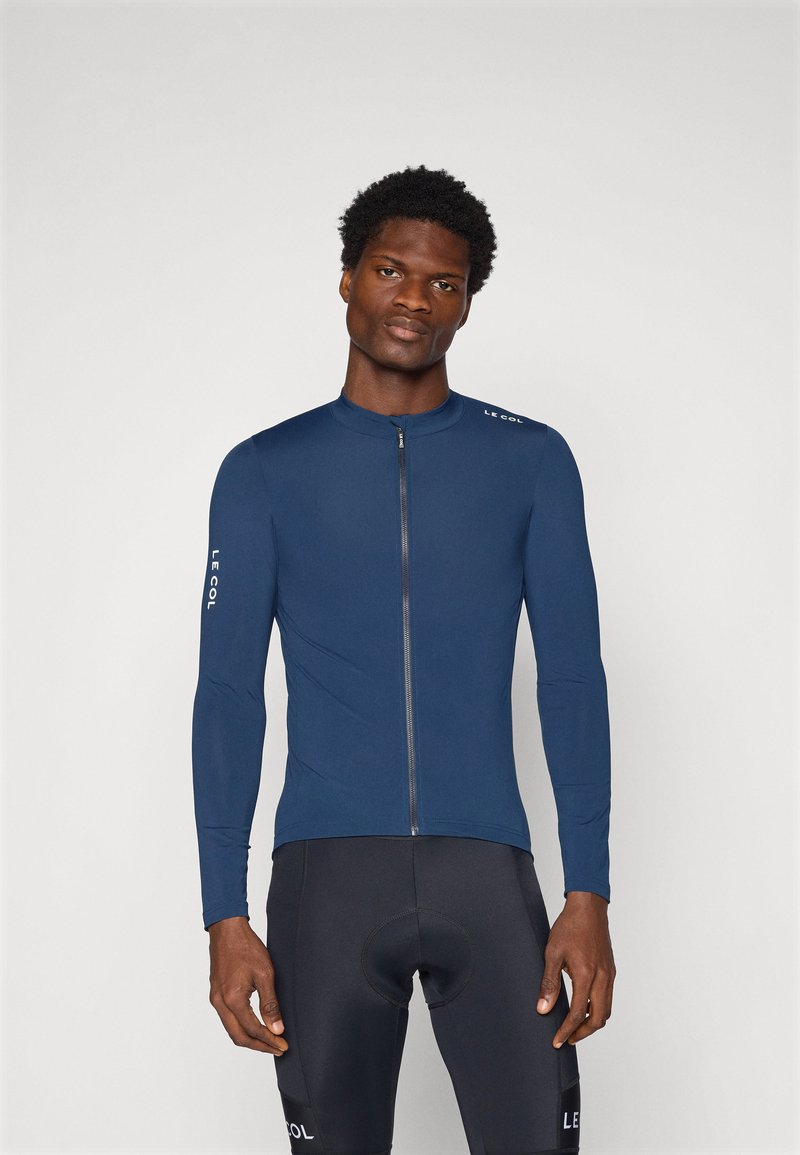 Maillot de cyclisme à manches longues marine avec un col haut, une fermeture éclair sur le devant et des accents de logo blancs. Matériel lisse et extensible pour le confort et la performance.