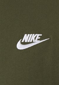 Tejido verde oliva con un tejido texturizado. Presenta un logo de Nike bordado en blanco con un diseño de swoosh curvado.