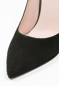 Gros plan sur une chaussure femme noire en daim à bout pointu avec une doublure intérieure rose clair.