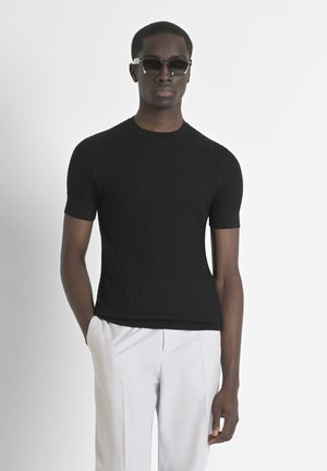 Black ribbed knit short-sleeve sweater with a crew neckline, worn with light-colored trousers. Texture is smooth and fitted.