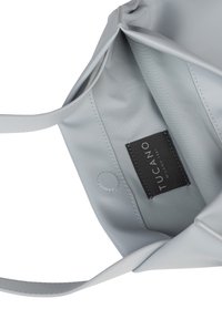Lichtgrijze tas met een glad leren buitenkant. Binnenkant heeft een stoffen voering en een zwart label met de branding "TUCANO".