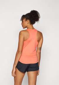 Lys korallfarget tanktop med racerback-design, laget av et glatt stoff. Sorte treningsshorts kompletterer antrekket, med en avslappet passform.
