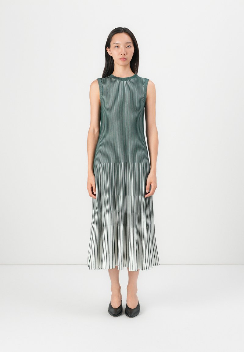 Pleated midi dress in shades of green, featuring vertical stripes, a round neckline, and sleeveless design. Shoes are pointed black heels.