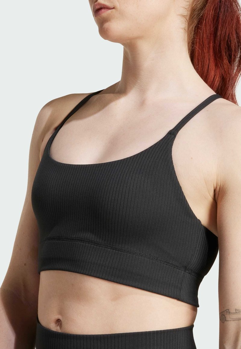 Sujeción deportiva negra con canalé que presenta tirantes finos y un diseño sin costuras, con un ajuste ceñido y un ligero estiramiento para mayor comodidad.