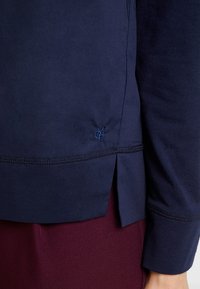 Marineblaue Sweatshirt mit langen Ärmeln, seitlichen Schlitzen, dezenten Steppdetails und einem gestickten Logo am Saum.