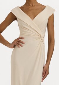Béžové zavinovací šaty s hlubokým V výstřihem a krátkými rukávy. Obsahují uzlový detail v pase, vyrobené z hladké, lehké tkaniny.