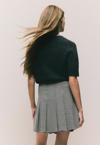 Čierny pletený sveter s krátkym rukávom v kombinácii s plisovanou sukňou v čierno-bielom vzoru houndstooth. Hladká textúra a priliehavý strih.