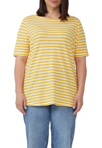Gelb-weiß gestreiftes T-Shirt mit kurzen Ärmeln, rundem Ausschnitt und lockerer Passform. Kombiniert mit locker sitzenden blauen Jeans.