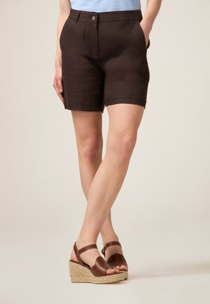 Brown linen shorts with a tailored fit, front pockets, and rolled hems, paired with brown leather wedge sandals and a light blue top.