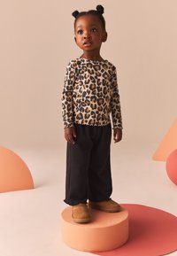 Long-sleeve, ribbed top with a leopard print pattern in beige and brown. Paired with black, loose-fitting pants and tan slip-on boots.