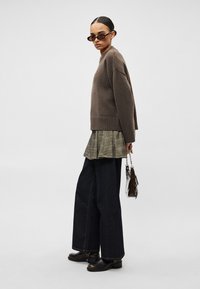 Καφέ πλεκτό πουλόβερ, φούστα με πλισέ σχέδιο σε καρό μο τίβο, σκούρο τζιν ψηλόμεσο, καφέ μποτάκια μέχρι τον αστράγαλο και μια μικρή γυαλιστερή τσάντα. Τα γυαλιά ηλίου ολοκληρώνουν το ντύσιμο.