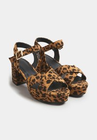Sandały na platformie w panterkę z szerokimi krzyżującymi się paskami, regulowanym paskiem na kostce i masywnym obcasem. Wykonane z miękkiego materiału przypominającego zamsz.