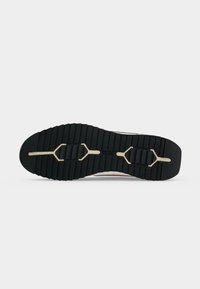 Semelle de chaussure en caoutchouc noir avec des rainures profondes, un motif central beige en forme de Y et le mot « BOSS » embossé au centre.