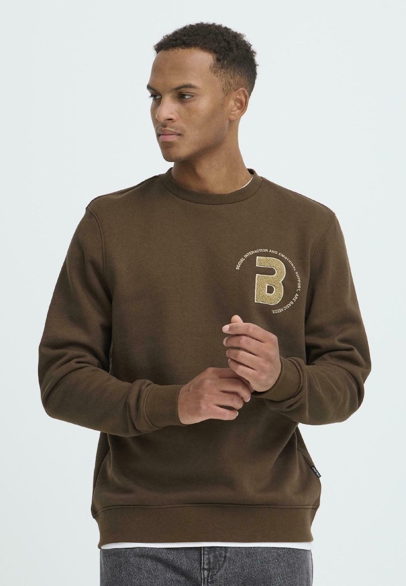 Bruine sweatshirt gemaakt van gestructureerde stof, met een ronde halslijn en een opvallend logo-detail op de linkerkant van de borst. Verstelbare manchetten.