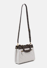 Sac à main en cuir blanc matelassé avec une bandoulière à motifs sombres, quincaillerie dorée et une poignée supérieure. Dispose d'une fermeture éclair et d'une forme structurée.