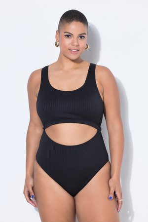 Kobieta z krótkimi włosami, ubrana w czarny prążkowany strój kąpielowy z wycięciami, złote kolczyki-koła, niebieski lakier do paznokci, uśmiechająca się na białym tle.