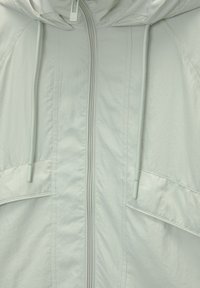 Světle šedá, kapucínková bunda s předním zipem, stahovacími šňůrkami a dvěma velkými kapsami; hladká textura a jemný lesk na látce.