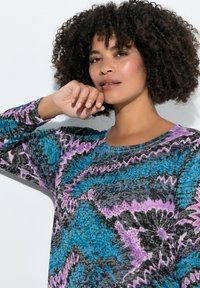 Langärmlige Tunika in lebhaftem Blau-, Lila- und Schwarzmuster, mit Rundhalsausschnitt und strukturiertem Stoff mit Akzentdetails.