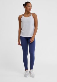 Vit athletic tank top med justerbara axelband, kombinerad med ribbade mörkblå leggings och vita löparskor. Enkel, funktionell design.