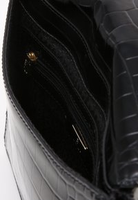 Borsa a mano in pelle nera con motivo a coccodrillo, dotata di più scomparti e di una tasca con cerniera. Interno in tessuto strutturato.