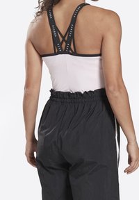 Light pink athletic top with black straps displaying “REEBOK” logo, paired with black, elastic-waist athletic pants featuring a textured finish.