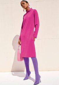 Fuchsia Kleid mit langen Ärmeln und hohem Kragen, mit Seitentaschen. Kombiniert mit knielangen lavendelfarbenen Stiefeln und einer rosa Handtasche. Glatte Textur.