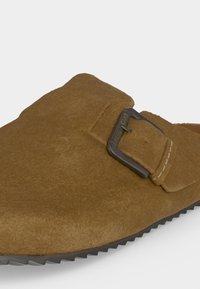 Καφέ σουέντ παπούτσι slip-on με ρυθμιζόμενο αγκράφα με την ένδειξη «PEPE JEANS» και ραβδωτή μαύρη σόλα, φαίνεται από την μπροστινή πλευρική γωνία.