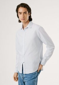 Gaiši zils garas piedurknes krekls ar plānu baltu un pasteļtoņu svītru rakstu, ar apkakli un nedaudz izliekta apakšmalu. Apvienots ar zilām džinsām.