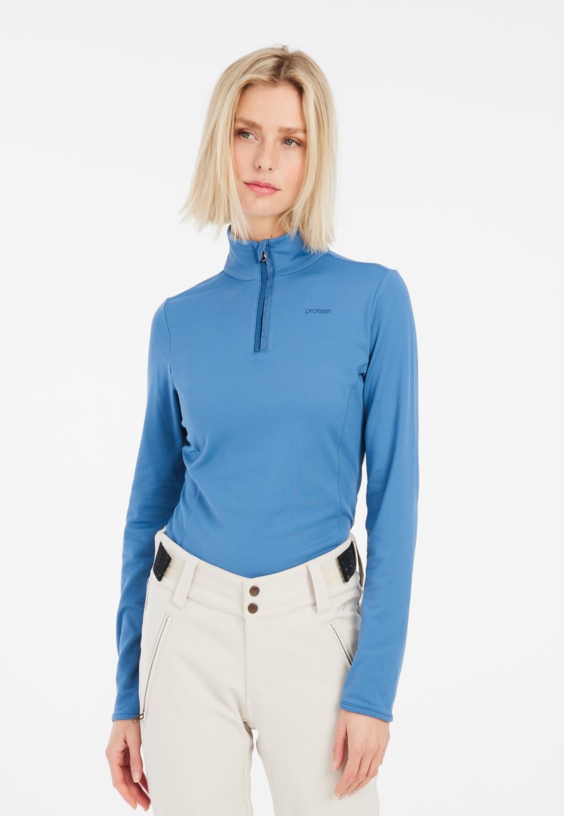 Maglione azzurro chiaro a maniche lunghe con zip e colletto alto, abbinato a pantaloni chiari con dettagli neri e tasche.